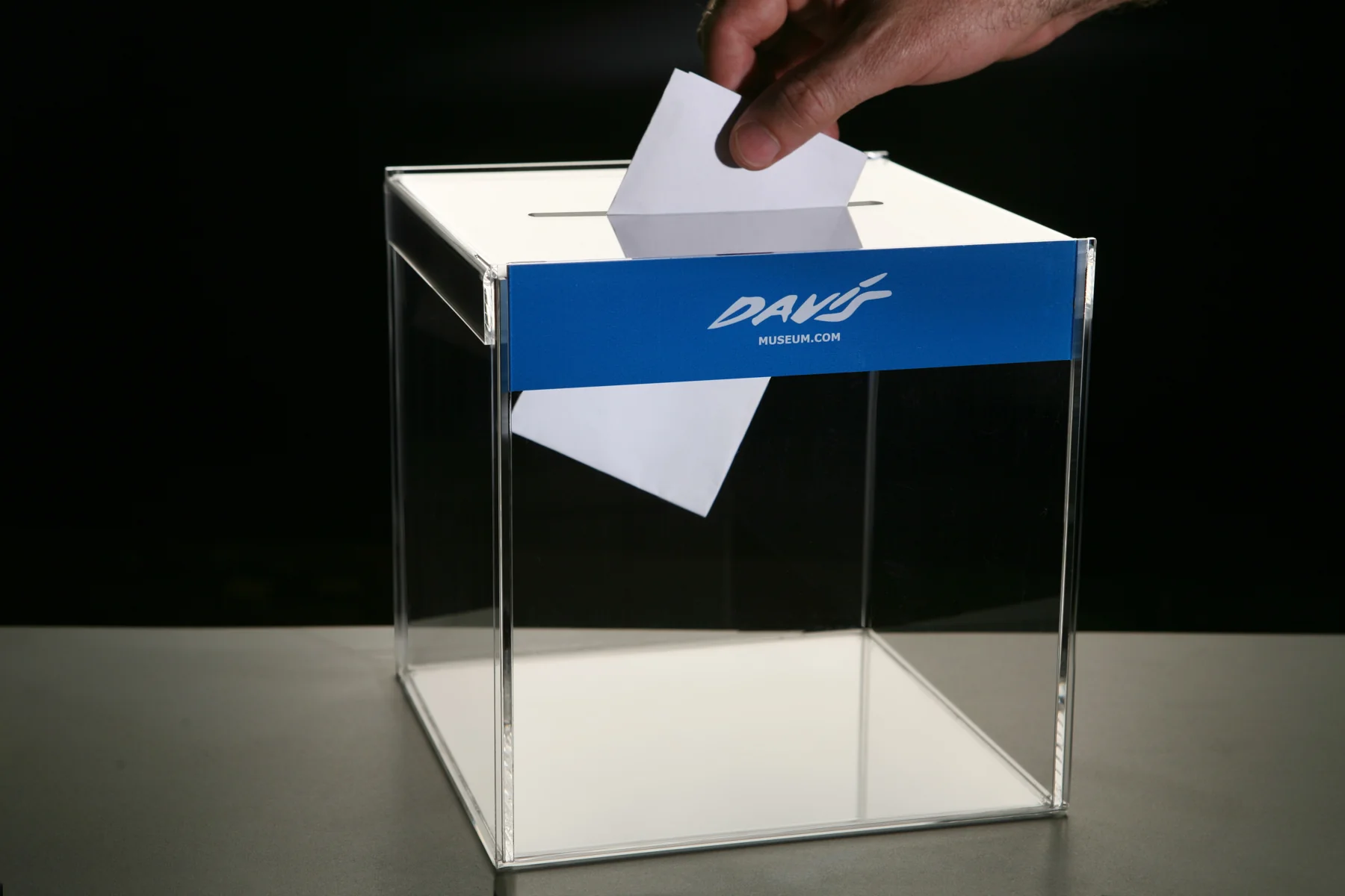 Una mano introduce una papeleta en una urna transparente